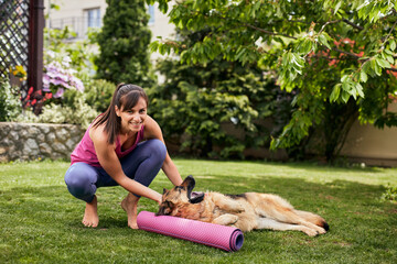 Young attractive fit yogi brunette playing with her dog in backyard.