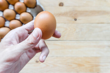 Man holding fresh chicken egg with copy space. Top view wooden table with paper panel background.