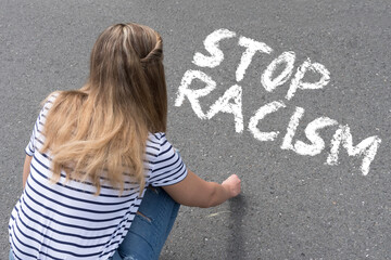 Eine junge Frau malt Slogan Stop Rassismus mit Kreide auf die Straße