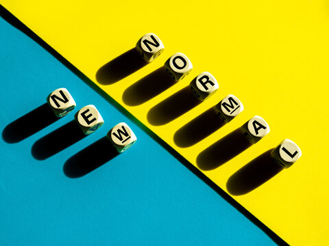 New Normal, word on wooden alphabet cube on blue and yellow background, minimal style.