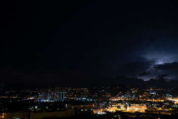Night landscape. Thunderstorm in the mountains above the night city. Light haze over the city lights.