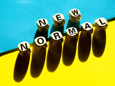 New Normal, word on wooden alphabet cube on blue and yellow background, minimal style.