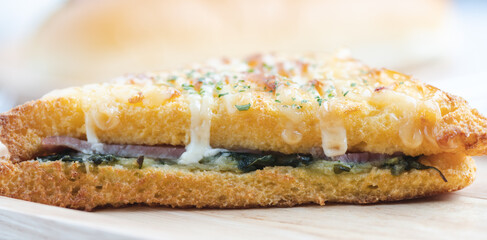 croque monsieur with slices of boiled ham, placed on a wooden plate with cooking tools.