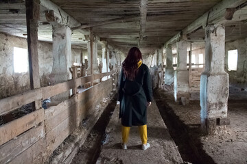  A girl in a gloomy abandoned building in a black cloak. Young woman in an industrial abandoned factory