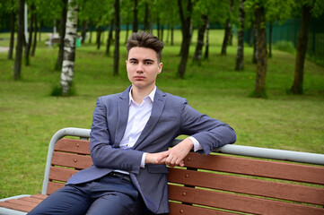 Obraz premium Portrait of a caucasian business man posing while sitting on a park bench. Photo taken in the spring.