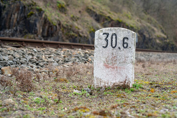 A white-painted milestone in front of a train track. Focus on the miletone, the track is blurred by...