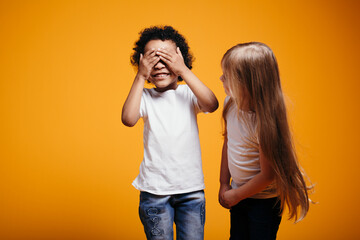 Long-haired girl child checks whether a dark-skinned boy peeps when playing hide and seek on an...