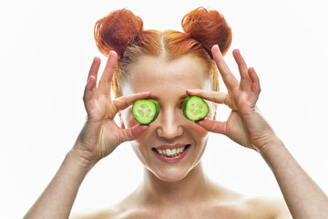 a close-up portrait of a red-haired girl with a green cucumber in her hands and next to her face. Isolated on a white background. - 355115624