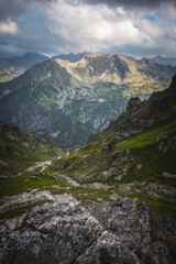 Mountain hiking trail lined with large gray stones covered with green moss surrounded by low mountain pine. In the distance visible high mountains and a steep path, curving among the rocks.