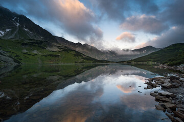 Fototapeta premium Ukryte jezioro z odbiciem gór w nim. Niskie chmury wiszące nad szczytami.