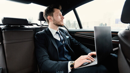 Young businessman using his laptop in luxury car