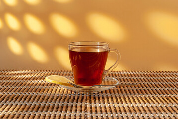 A cup with tea and a slice of lemon stands on a table covered with a mat against the backdrop of...
