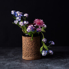 A small bouquet of forget-me-nots and daisies in a ceramic glass on a dark background