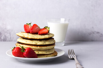 Delicious homemade pancakes with strawberries and a glass of milk in the background on a light background.