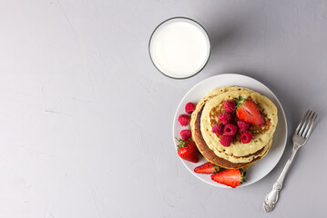 Homemade pancakes with strawberries and raspberries and a glass of milk - a delicious breakfast, a light background.
