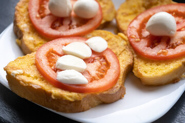 Toasts with fresh sliced tomato and mozzarella on the white plate for breakfast in the morning. Vegetarian meal. Close-up. Side view