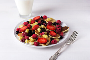 Mini pancakes with strawberries, raspberries and currants and a glass of milk - a delicious breakfast. A close-up