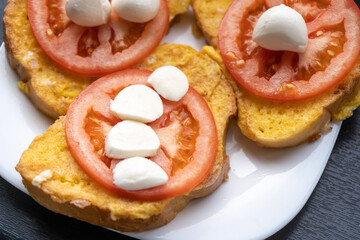 Toasts with fresh sliced tomato and mozzarella on the white plate for breakfast in the morning. Vegetarian meal. Close-up