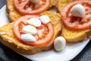 Toasts with fresh tomato and mozzarella on the white plate for breakfast in the morning. Vegetarian meal. Close-up