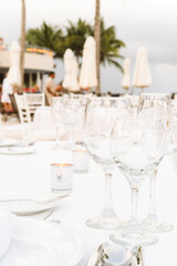 Festive serving with glasses for an outdoor celebration with garland lamps and palms at the background. Wedding, anniversary, birthday dinner and party. Toned image with place for text