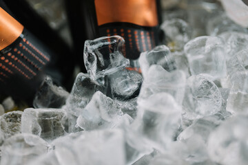 Ice cubes close up with bottles of champagne in an ice vase
