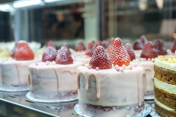 Cakes with strawberries and cream on a cafe showcase behind glass