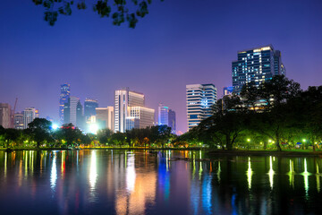 Fototapeta na wymiar Bangkok city at night - Architecture of capital city. Landscape night view of illuminated skyscrapers buildings on skyline and their reflection in lake water in Lumphini park in Bangkok, Thailand