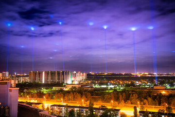 Night illuminated city with blue lights in the clouds and sky
