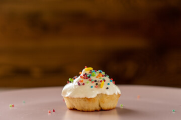Festive Easter cupcake with icing and colorful dragees on the left on a pink plate on the wooden background
