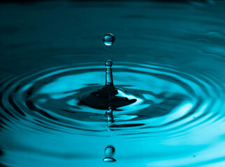 Water drop falling through the air. Small round ripples in a smooth surface and a reflection