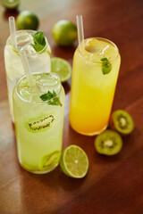 lemonade cocktails in glasses with straws and limes on wooden table, close view