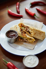white plate with mexican burrito and peppers with sauce on wooden table, close view 