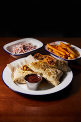 white plate with mexican burrito and bowls with snacks on wooden table, close view 
