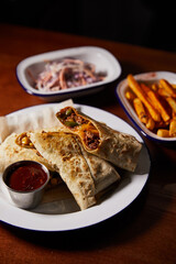 white plate with mexican burrito and bowls with snacks on wooden table, close view 