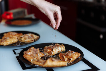 Woman's hand decorates pancakes with a chocolate, fruits kiwi and banana. Black plate, white table