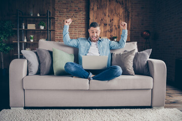 Obraz premium Full body photo of handsome homey guy relaxing sitting comfy couch legs crossed browsing notebook freelancer remote work stay home quarantine got big salary living room indoors