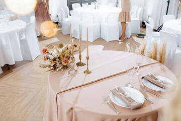 Romantic table setting in a restaurant for a holiday. Wedding decor for newlyweds at a banquet. Dried flowers floristry and candles, boho style. Cartering service for the bride and groom and guests.
