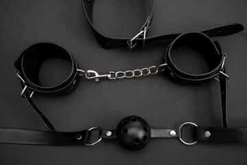 Leather whip, handcuffs and gag on black background. Top view