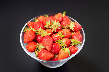 Fresh organic strawberries in a glass bowl  on a black table. Soft focus.