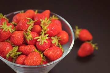 Fresh organic strawberries in  glass bowl and several berries on dark table.