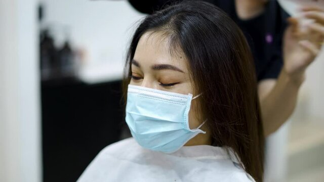 hairdresser cutting the hair to a female client, people must be wering medical mask to protection coronavirus (covid-19) pandemic. new normal concepts