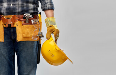 repair, construction and building - male worker or builder with helmet and working tools on belt over grey background