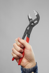 repair, construction and building tools concept - close up of builder's hand holding adjustable wrench over grey background