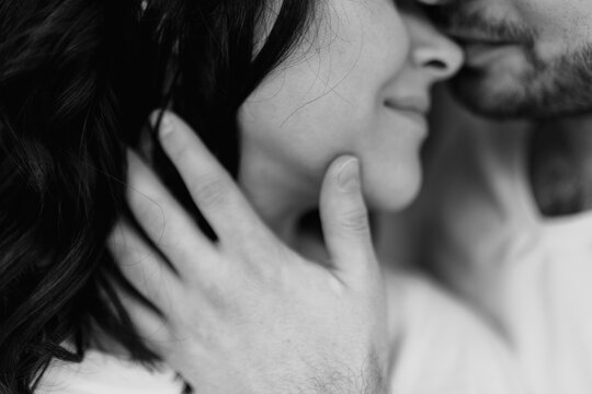 Selected soft focus on a hand. Close up cropped portrait of a couple in love together at home. Bearded brunette man gently touch with his hand face of her young dark long hair woman. Black and white
