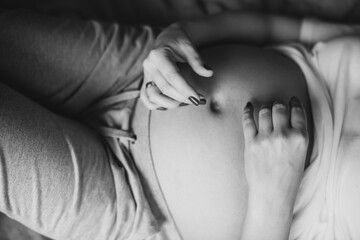 Beautiful Pregnant Woman Holding Hands on Belly while laying. Waiting for Baby. Pregnant Young Girl. Healthcare Concept. Relaxing at Home. Care of Pregnant. Indoor Rest.