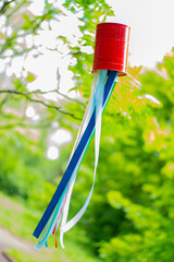 Colorful ribbons blowing in the wind hang down from metal can attached to the tree in the park during recycling Festival on blurred green plants background