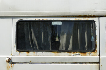 Car window with dirty curtains in a white rusty abandoned compact van. Unnecessary faulty car thrown on the side of the road.