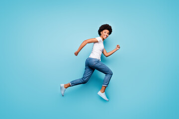 Fototapeta na wymiar Full body photo of funky dark skin curly lady jumping high rushing marathon finish line coming first active sporty person wear casual white t-shirt jeans isolated blue color background