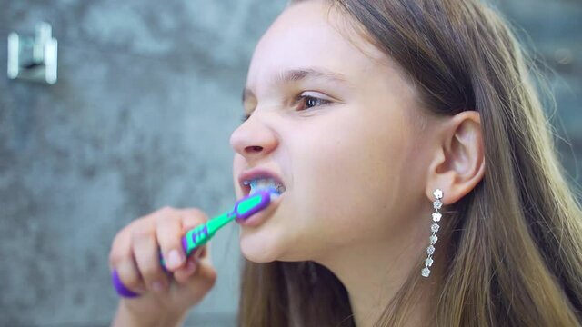 Portrait happy cute young teenage girl brushing teeth in bathroom and smiling. Children daily healthcare routine. Caucasian kid with white tooth looking at mirror isolated at home. Lifestyle.