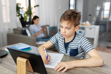 children, education and school concept - student boy with tablet pc computer and test learning online at home